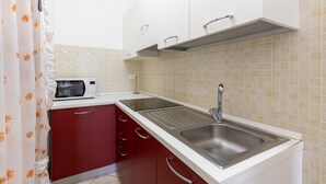 A kitchen with white cabinets, a stainless steel sink, a microwave, and a tiled backsplash.