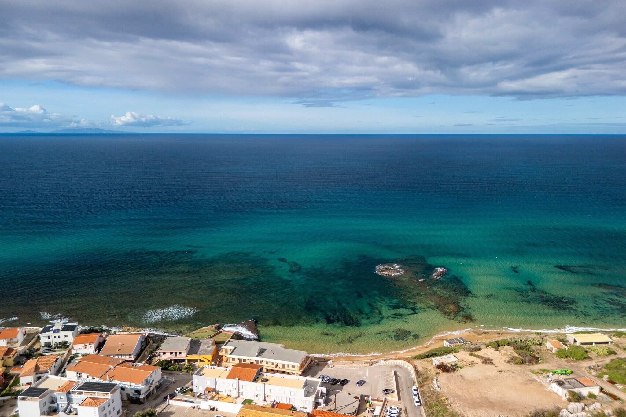 Une vue aérienne d’une ville côtière, avec des bâtiments le long de la côte, une vue dégagée sur l’océan et une plage de sable.