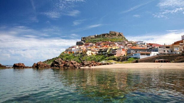 A coastal town with clear waters, a sandy beach, and buildings on a hill.