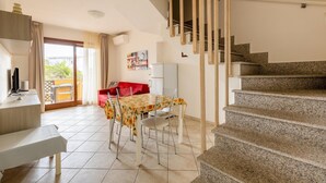 A dining area with a table and chairs, a kitchen area with a refrigerator, and a staircase leading to an upper floor.