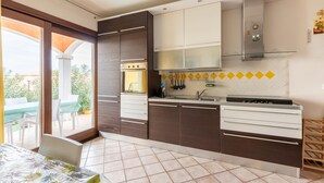 A modern kitchen with dark brown cabinets, a stainless steel range hood, and a glass backsplash. - Apt con giardino, a 300-metre-tall mare (Lu Bagnu)