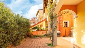 A courtyard with a brick pathway, a staircase, and a building with yellow walls and an arched entrance. - Apt con giardino, a 300-metre-tall mare (Lu Bagnu)