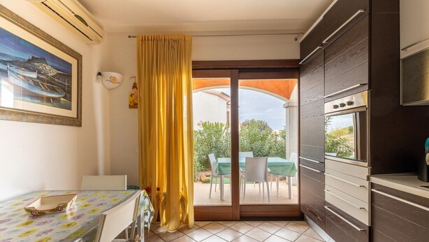A compact kitchen with a sliding glass door leading to an outdoor dining area. - Apt con giardino, a 300-metre-tall mare (Lu Bagnu)