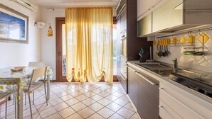 A kitchen with a dining area, a window with curtains, and a tiled floor. - Apt con giardino, a 300-metre-tall mare (Lu Bagnu)