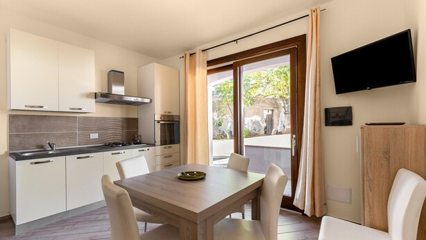 A modern kitchen with a dining area, a TV mounted on the wall, and a view of the outside. - Air-conditioned with garden and private parking (Badesi)