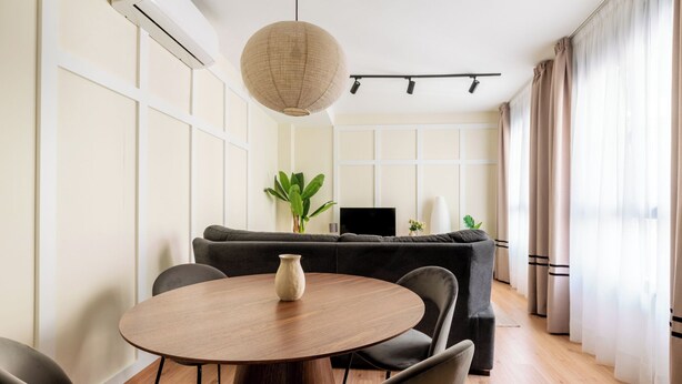 Een moderne woonkamer met een ronde houten eettafel, grijze banken en een hanglamp.