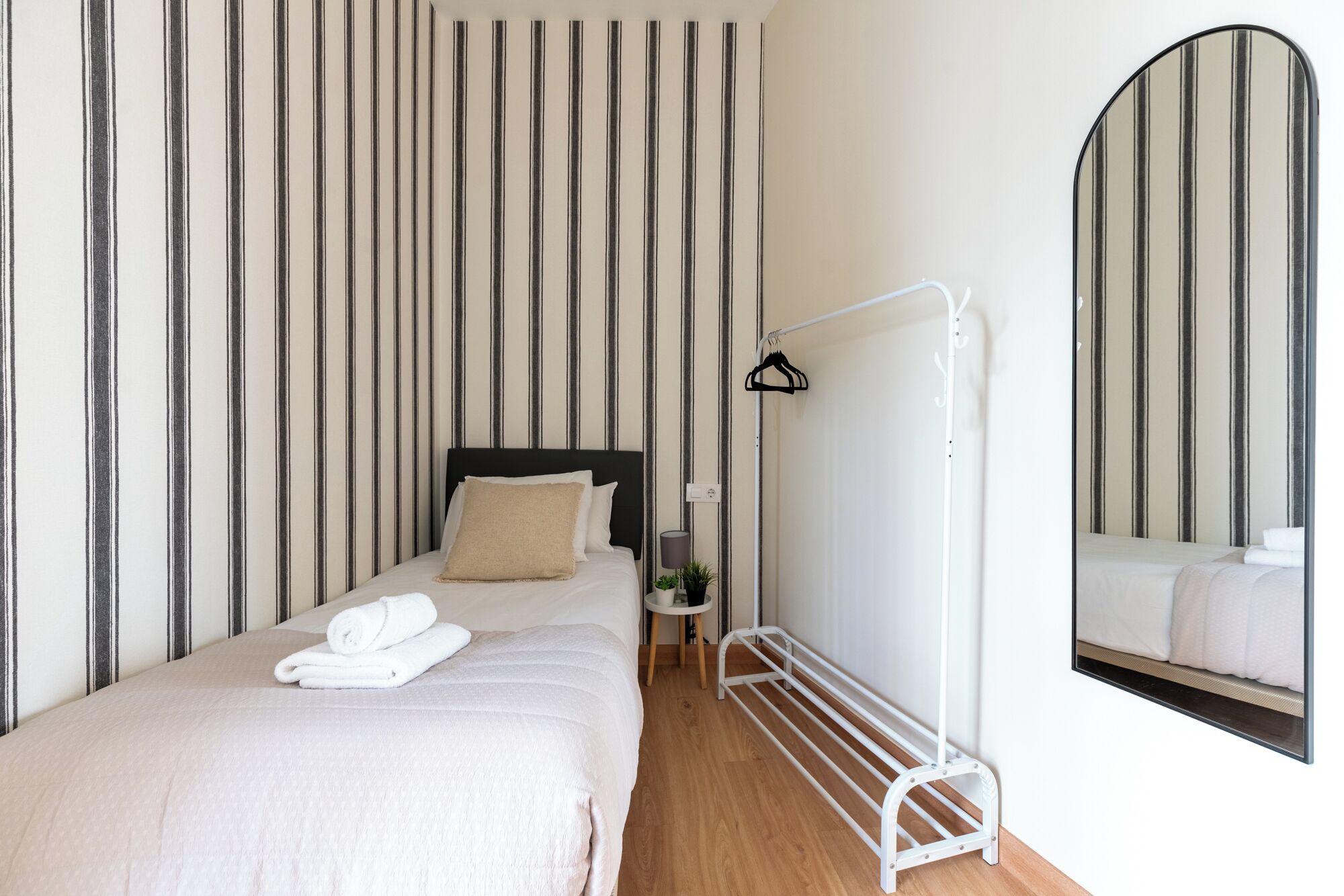 Un lit simple avec une tête de lit noire, une table de chevet avec une lampe et un miroir au mur.