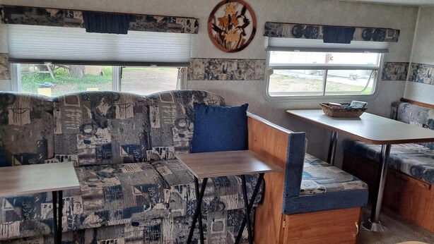 A compact RV interior with a sofa, two dining tables, and a small kitchenette area. - Comfortable RV in rural area - West Richland (West Richland)