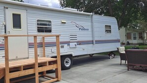 A Pioneer RV with a wooden bench and a small table in front, parked on a driveway. - Comfortable RV in rural area - West Richland (West Richland)