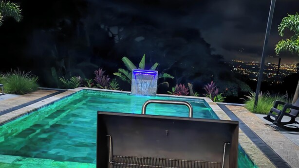 A barbecue grill with food, a pool, and a night view of a cityscape.