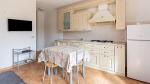 Una cocina con mesa, sillas, televisor y refrigerador.