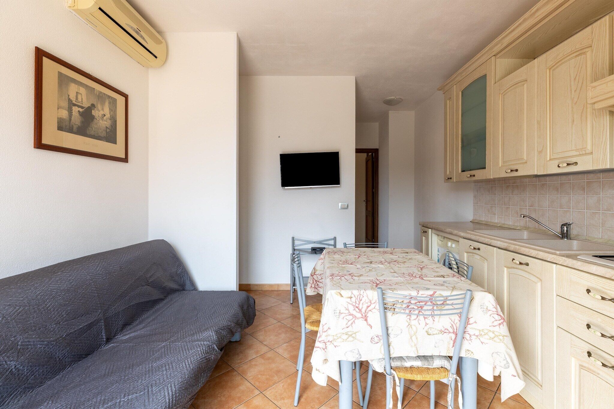 Cocina compacta con una mesa de comedor, sillas, un sofá y un televisor de pantalla plana montado en la pared.