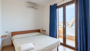 Un dormitorio con cama, mesita de noche, aire acondicionado instalado en la pared y puerta corrediza de vidrio a un área exterior.