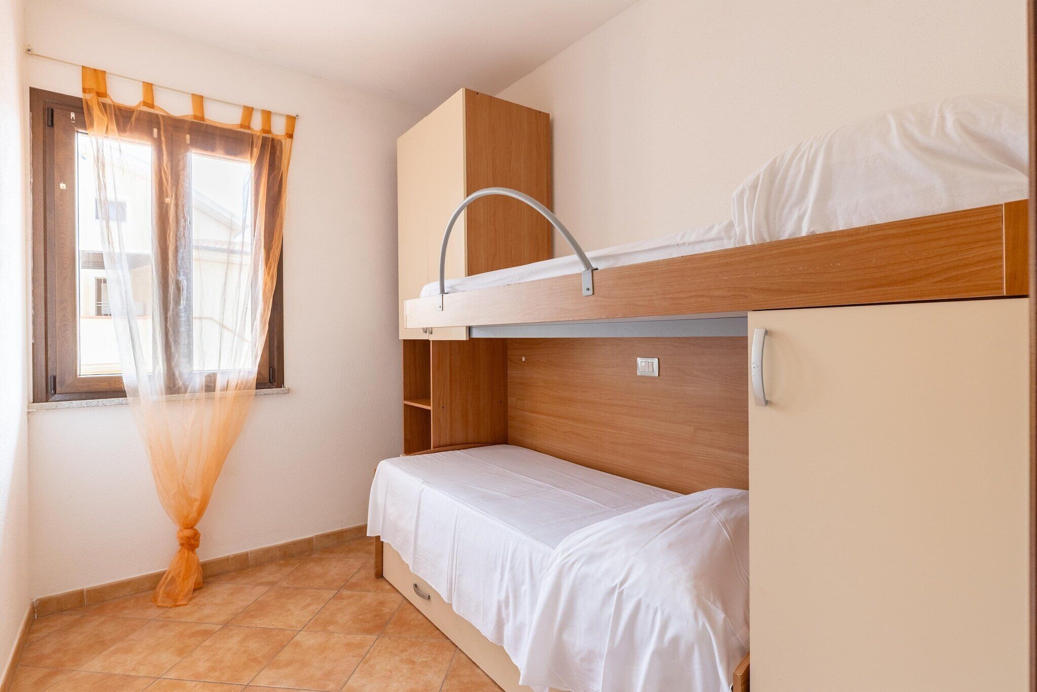 A bunk bed room with a window, curtains, and a wooden wardrobe.
