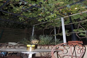 Un espace extérieur aménagé avec des tables et des chaises, entouré de verdure et surmonté d’une structure métallique.