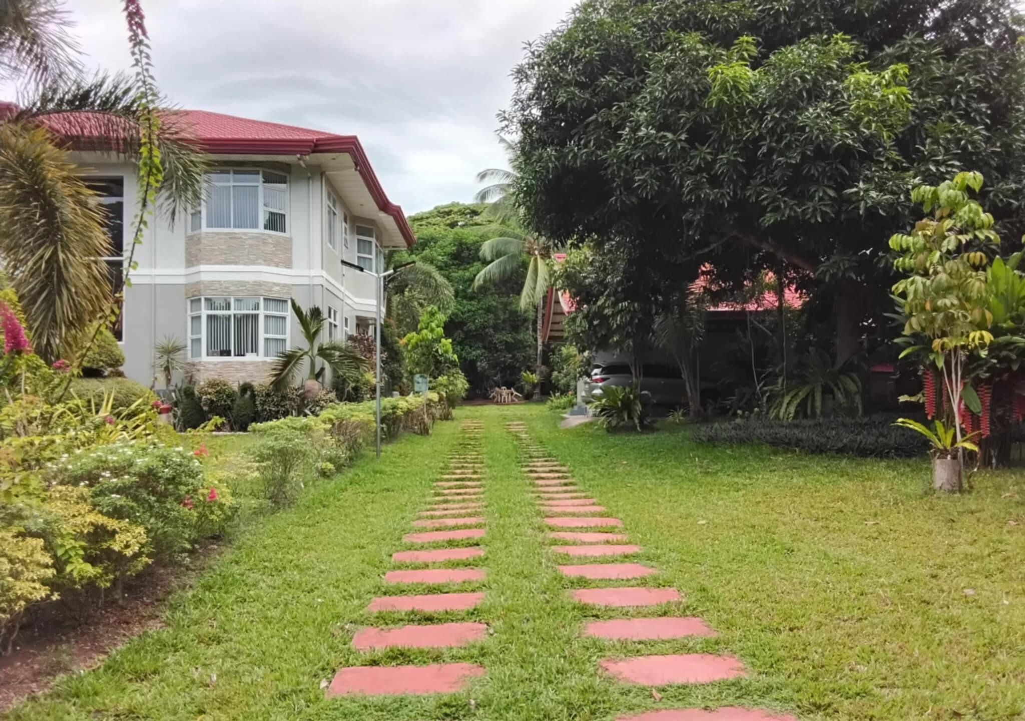 A house with a red roof, surrounded by lush greenery and a stone pathway leading to the entrance.
