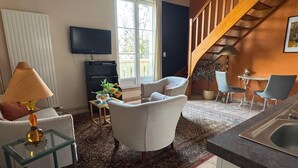 Una sala de estar con sofá, sillones, televisor, escalera y área de cocina.