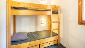 A bunk bed with a wooden frame, a mattress, a pillow, and two wall-mounted lights. - Two-Room Alpine Base for 5 (Risoul)