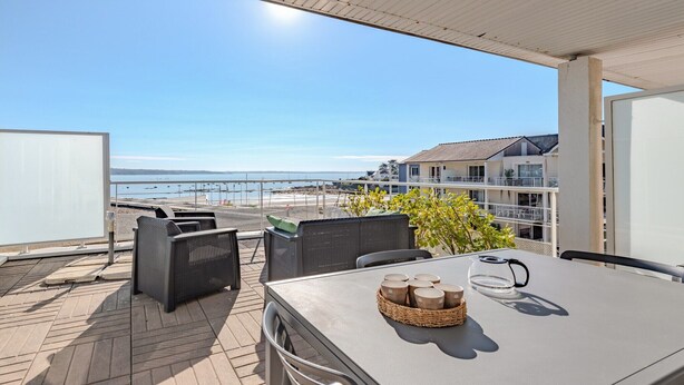 A balcony with a table and chairs, overlooking a beach and buildings.