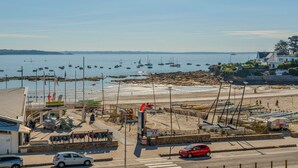 A coastal marina with boats docked, a sandy beach, and a road with cars.