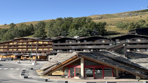 A multi-story hotel with a ski resort backdrop, featuring a prominent ski lift and a mountain view. - 3-bedroom apartment for six guests (Les 2 Alpes)