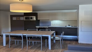 A compact kitchen with a microwave, stove, and sink. There is a dining table with chairs and a hanging light fixture. - 3-bedroom apartment for six guests (Les 2 Alpes)