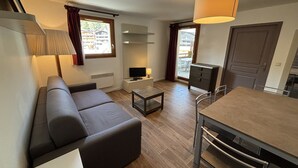 A modern living room with a sofa, a TV, a small table, and a dining area with a table and chairs. - 3-bedroom apartment for six guests (Les 2 Alpes)