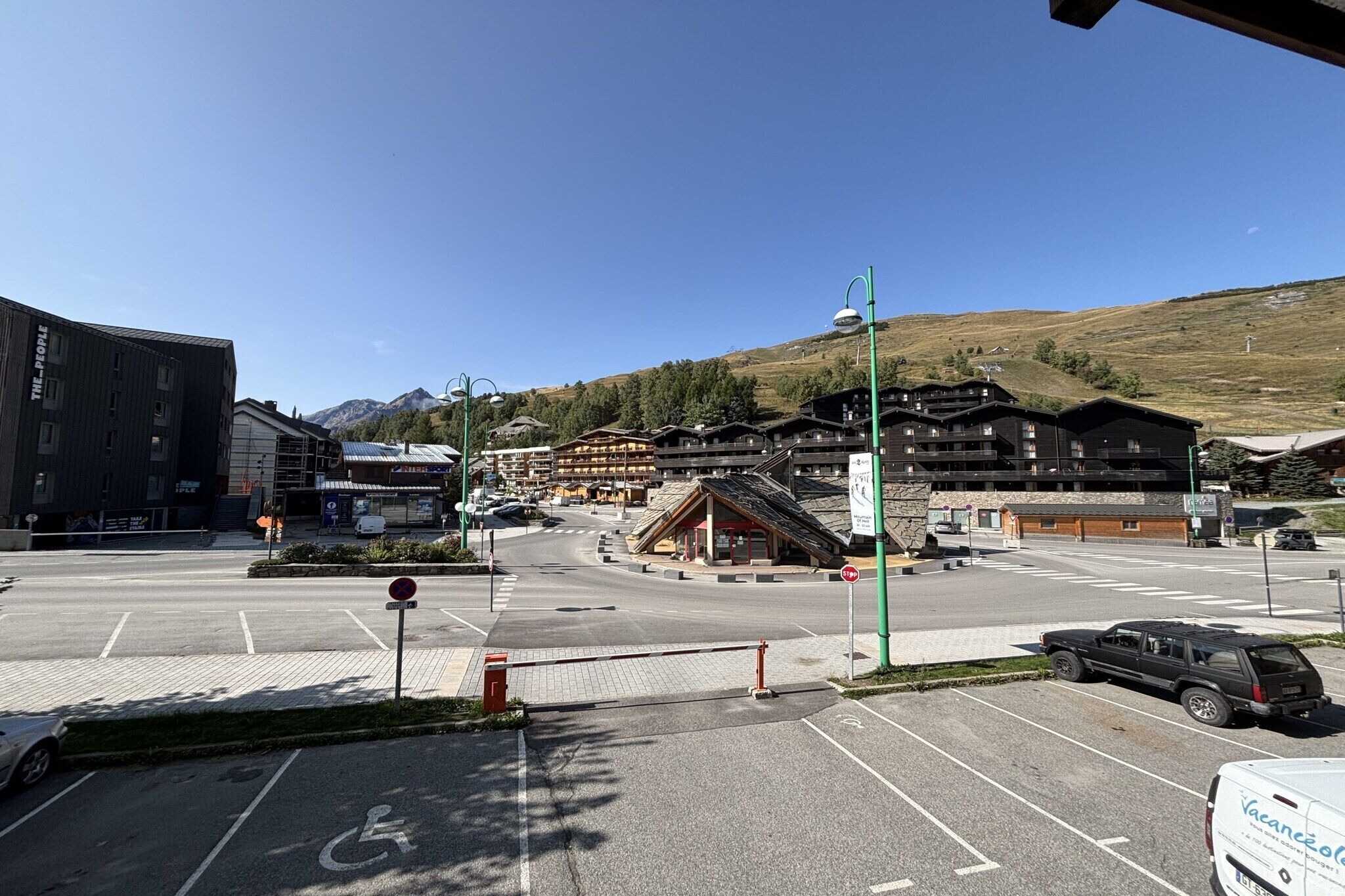 A parking lot with a stop sign, a building with a ski lift, and a mountain in the background.