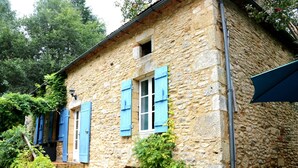 Un edificio de piedra con contraventanas azules, una escalera y una pequeña ventana.