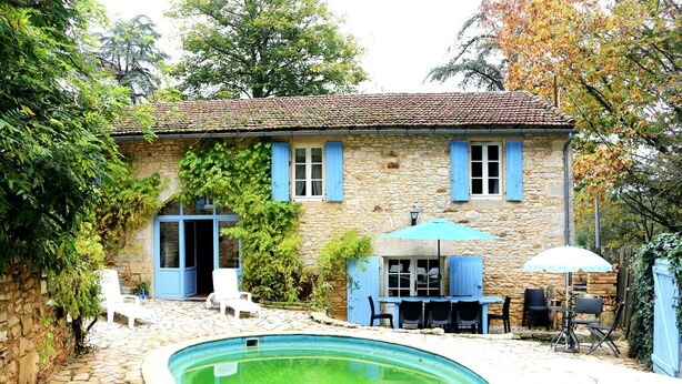 Una casa de piedra con piscina, mobiliario exterior y un patio cubierto.