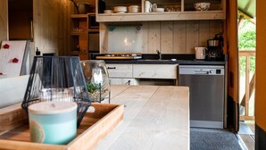 A wooden interior with a kitchen area, including a stove, sink, and shelves with dishes. - Luxury Family Tent with Play Area (Balkbrug)