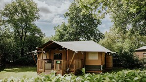 A small wooden cabin with a porch, a small deck, and a covered outdoor area. - Luxury Family Tent with Play Area (Balkbrug)