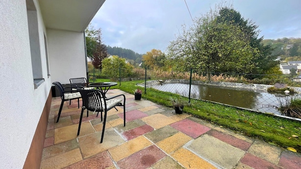 Ein Balkon mit Tisch und Stühlen, Blick auf einen Fluss und eine begrünte Fläche mit Bäumen.