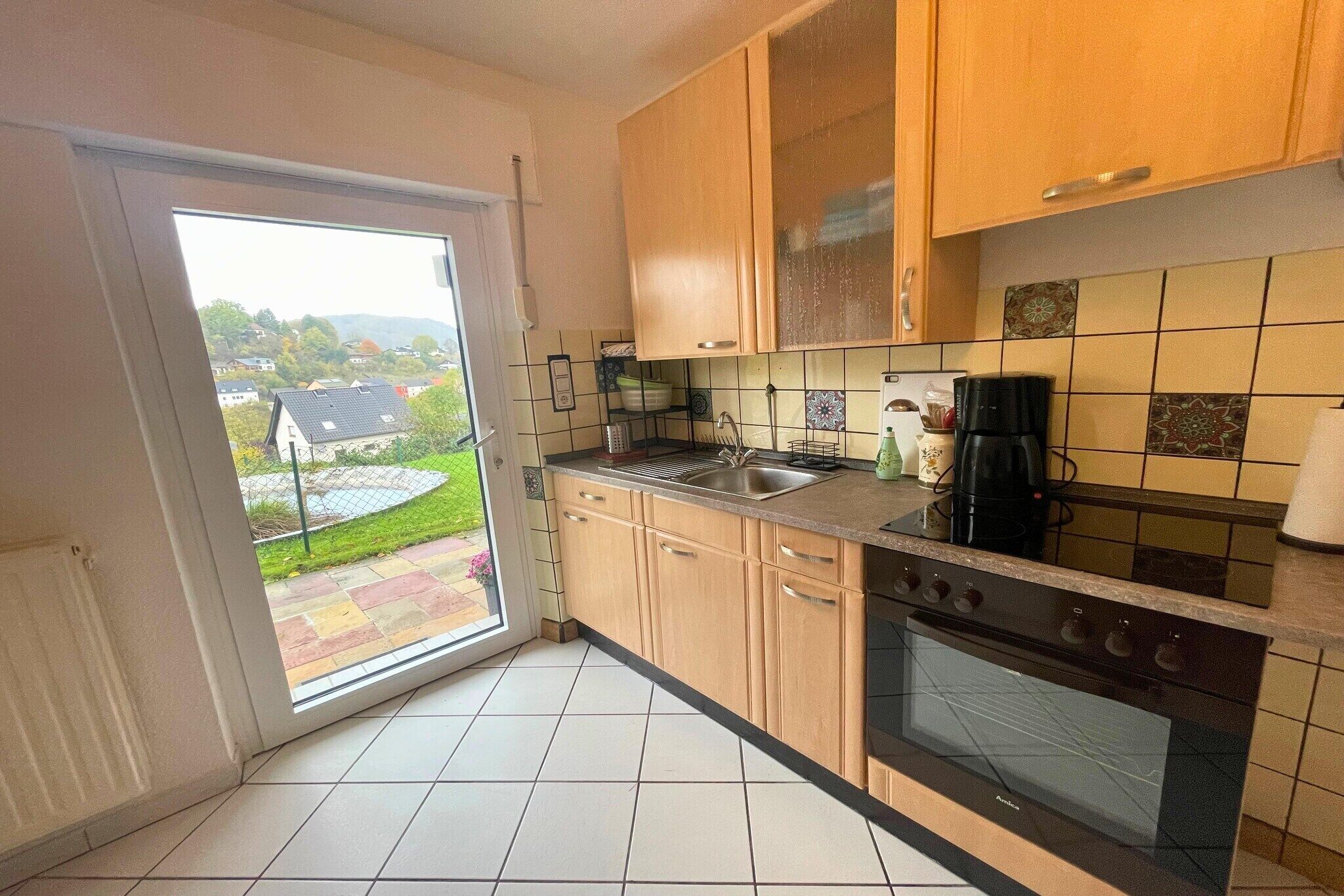 A kitchen with wooden cabinets, a black stove, and a window overlooking a garden.