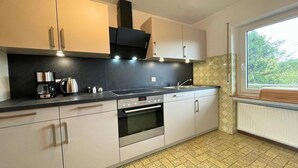 A modern kitchen with a built-in oven, a coffee maker, and a window with a view of greenery. - Holiday Home in Birresborn with balcony (Birresborn)