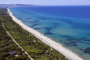 An aerial view of a coastal area with a long sandy beach, clear blue waters, and dense greenery along the coastline. - Air-conditioned apartment with private parking (Badesi)