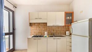Une cuisine de taille réduite avec des meubles blancs, un pare-feu en carrelage, un évier, une cuisinière et un réfrigérateur.