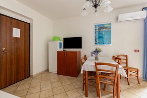A dining area with a table, chairs, a television, a cabinet, and a wall-mounted air conditioner.