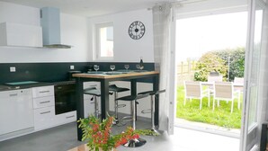 Una cocina moderna con armarios blancos, horno empotrado y comedor con mesa de madera y taburetes de bar.