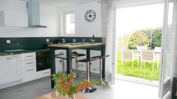 Une cuisine moderne avec des meubles blancs, un four encastré et un coin repas comprenant une table en bois et des tabourets de bar.