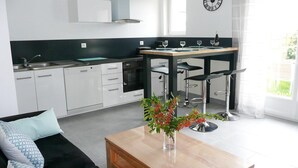 Una cocina moderna con armarios blancos, encimera negra y una zona de comedor con dos taburetes de bar.