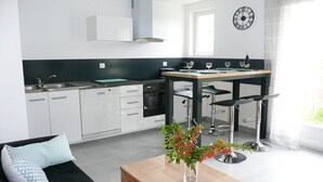 Cocina moderna con armarios blancos, encimera negra y comedor con mesa de madera y taburetes de bar.