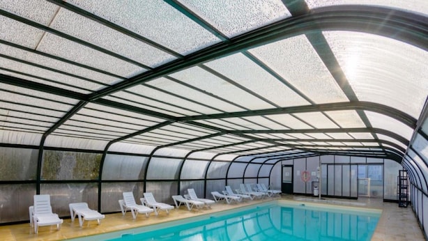 An indoor swimming pool with a curved roof, white lounge chairs, and a clear glass ceiling. - Peaceful coastal stay with access to pool (Saint-Nic)