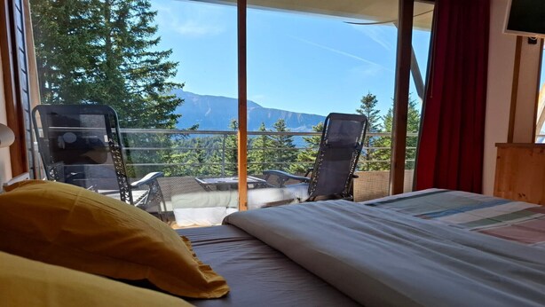 Une chambre avec un lit, deux chaises et un balcon offrant une vue sur la montagne.