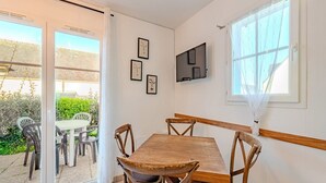 Un coin repas avec une table en bois et quatre chaises, un téléviseur fixé au mur et une fenêtre avec un rideau.