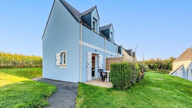 Une maison à deux étages, avec un toit en pente, une porte d’entrée et un petit patio agrémenté d’une table et de chaises.