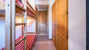 A narrow hallway with bunk beds on one side and wooden doors on the other.
