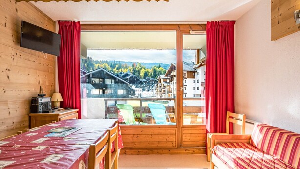 A wooden room with a bed, a sofa, a TV, and a table with a lamp.