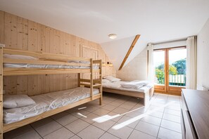Ein Schlafsaalzimmer mit drei Holzbettstegen, einem kleinen Schreibtisch und einem Fenster mit Blick auf Grünflächen.