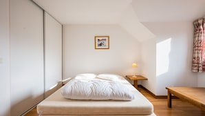 A bedroom with a bed, a bedside table with a lamp, a wooden bench, and a picture on the wall. - Bright family apartment with balcony (Giez)